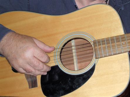 Close-up of body and strings of an acoustic guitar being strummed by a masculine hand.  Bordered Page size 3000 x 2250px (300ppi).  Actual image size 10 x 7.5.